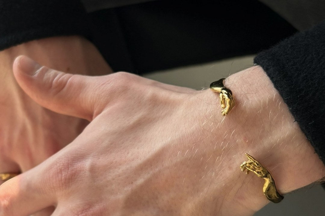 Gold Creation of Adam cuff on a man's wrist, the two hands almost touching